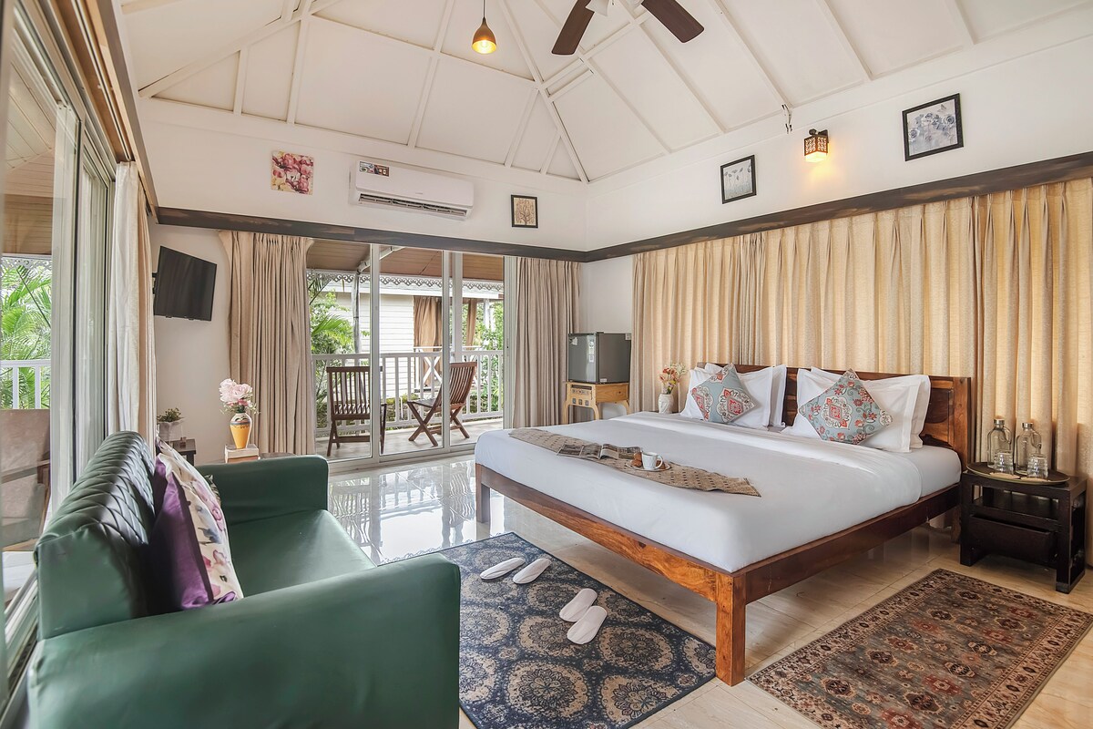 A spacious bedroom with a large bed, a green armchair, and a view of the outdoors through a sliding door.