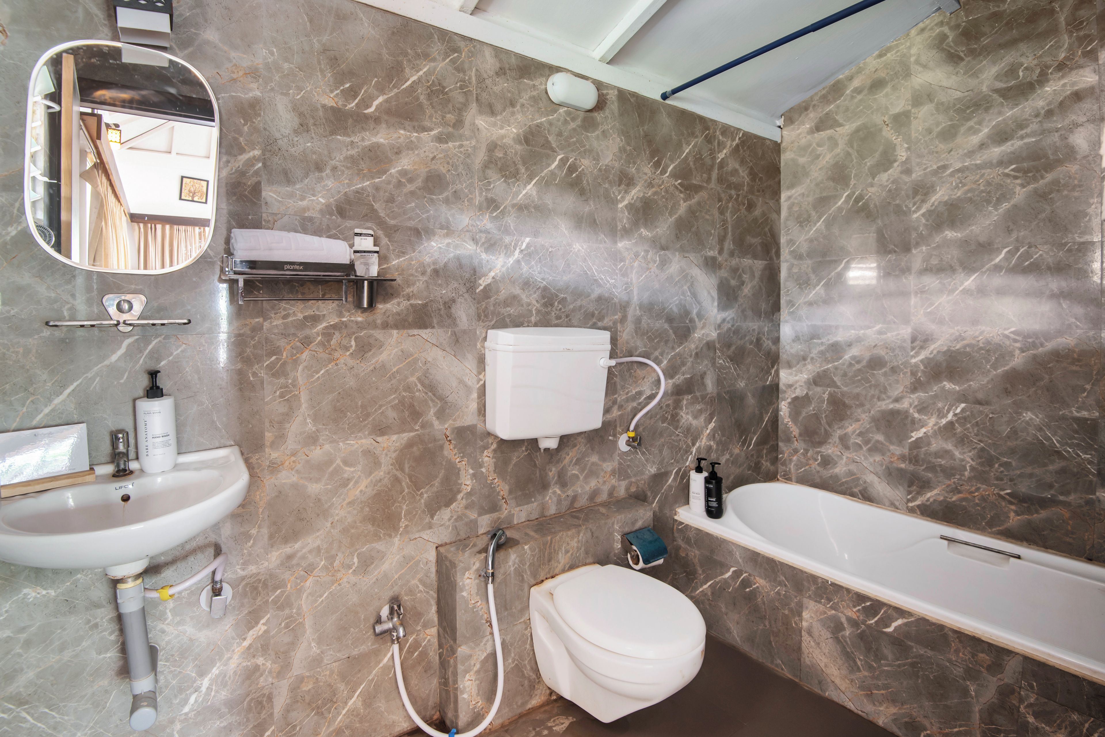 Une salle de bain avec un lavabo, des toilettes et une baignoire blancs, des murs en marbre et un miroir.