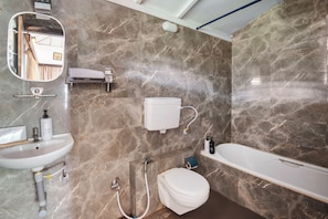 A bathroom with a white sink, toilet, and bathtub, marble walls, and a mirror.