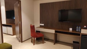 Een hotelkamer met een televisie aan een houten paneelwand, een bureau met een stoel en een prullenbak.