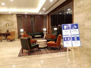 Un hall d’hôtel aménagé avec des espaces pour s’asseoir, un comptoir d’enregistrement et des panneaux d’information.