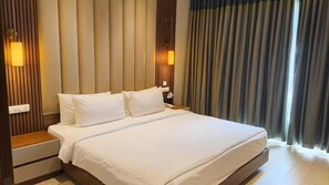 Une chambre d’hôtel avec un grand lit, une tête de lit en bois, deux tables de chevet et une vue sur l’extérieur à travers des rideaux.