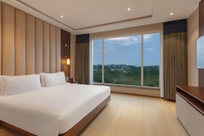 A hotel room with a large bed, a TV, a desk, and a window with a view of the city. - Fortune Park Airport Road Hubballi (Hubli)