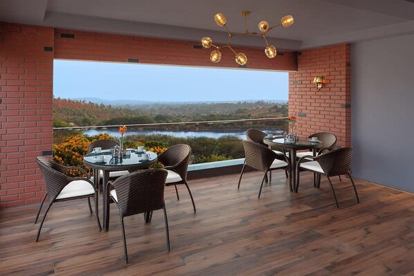 Un coin repas offrant une vue sur un lac et des collines, avec des chaises en osier et une table en verre.