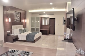 A modern hotel room with a large bed, bedside tables, a flat-screen TV, a mirror, and a wardrobe.