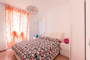 Quarto com cama, mesa de cabeceira, luminária pendente e janela com cortinas.
