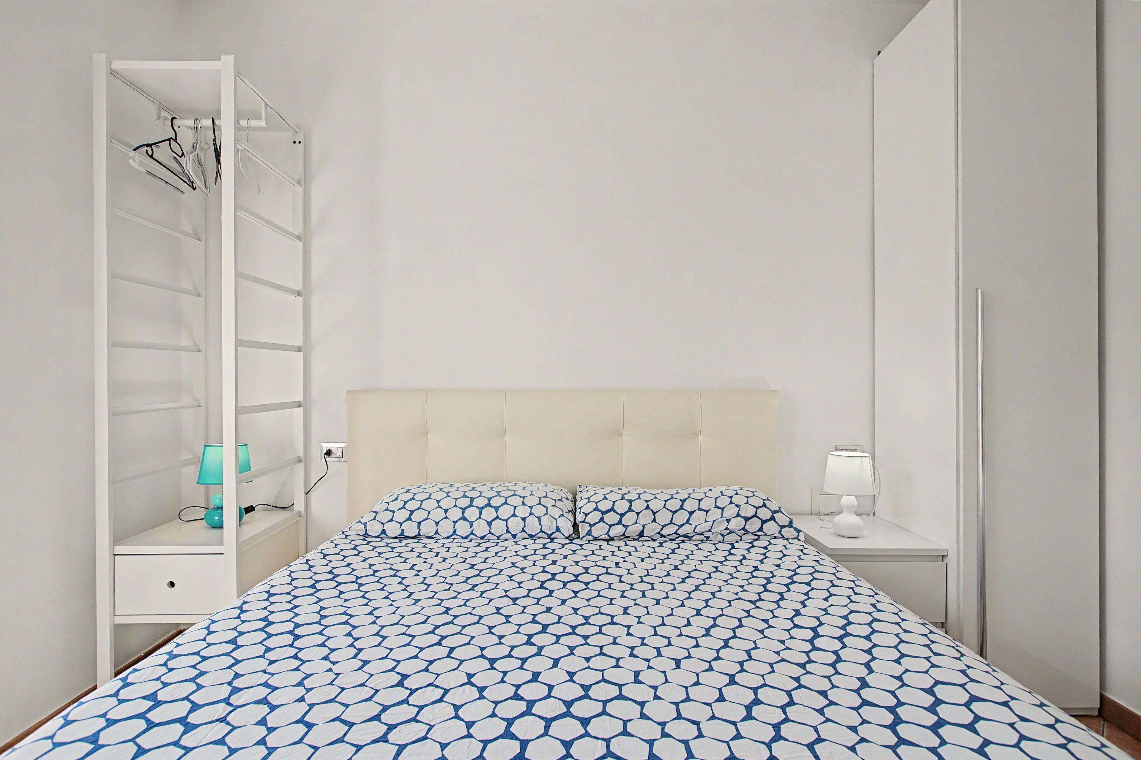 Un dormitorio con cama, armario, mesita de noche y velador.