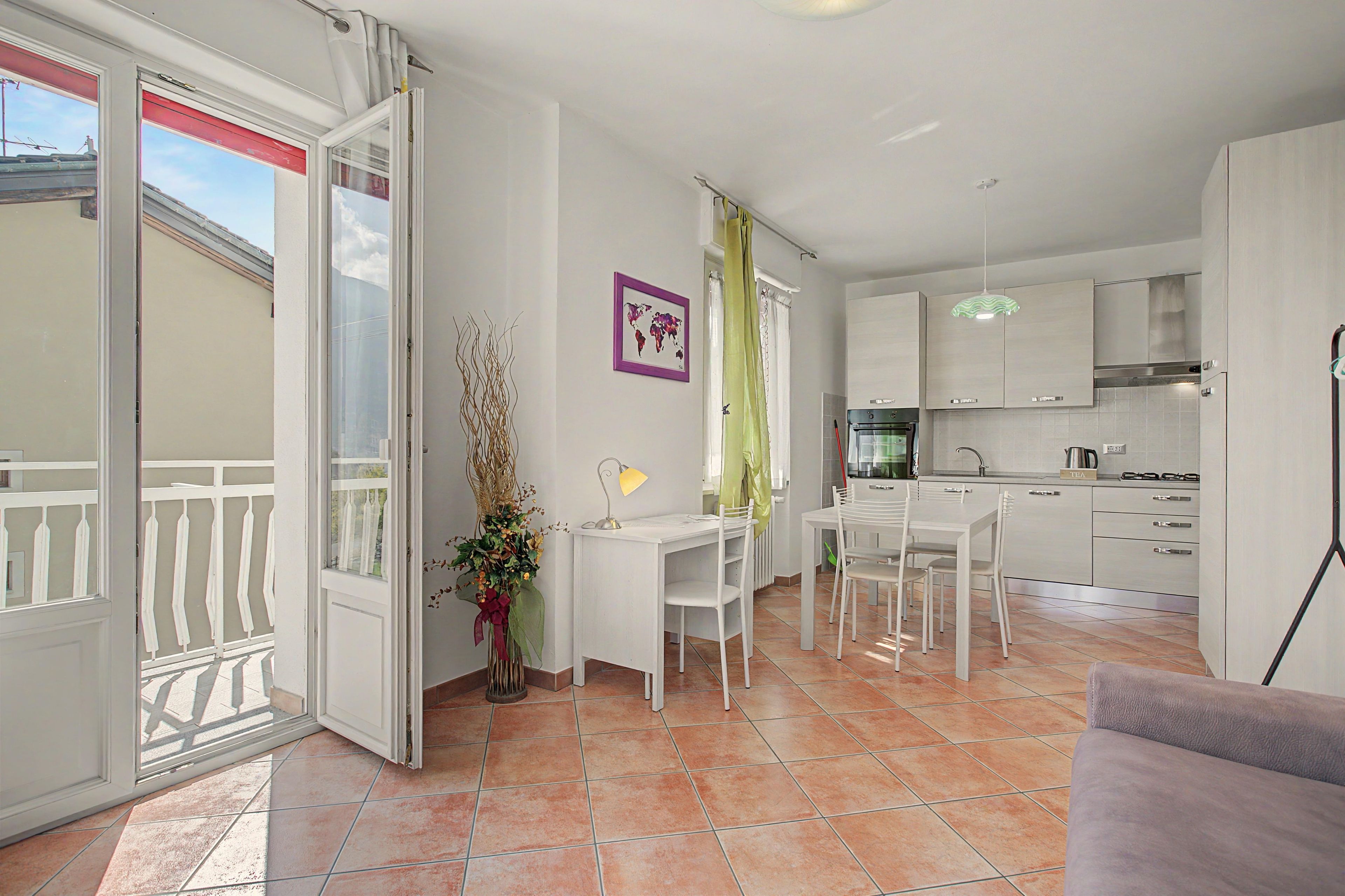 Une cuisine moderne avec des meubles blancs, un coin repas avec des chaises blanches et un balcon doté d’une balustrade blanche.