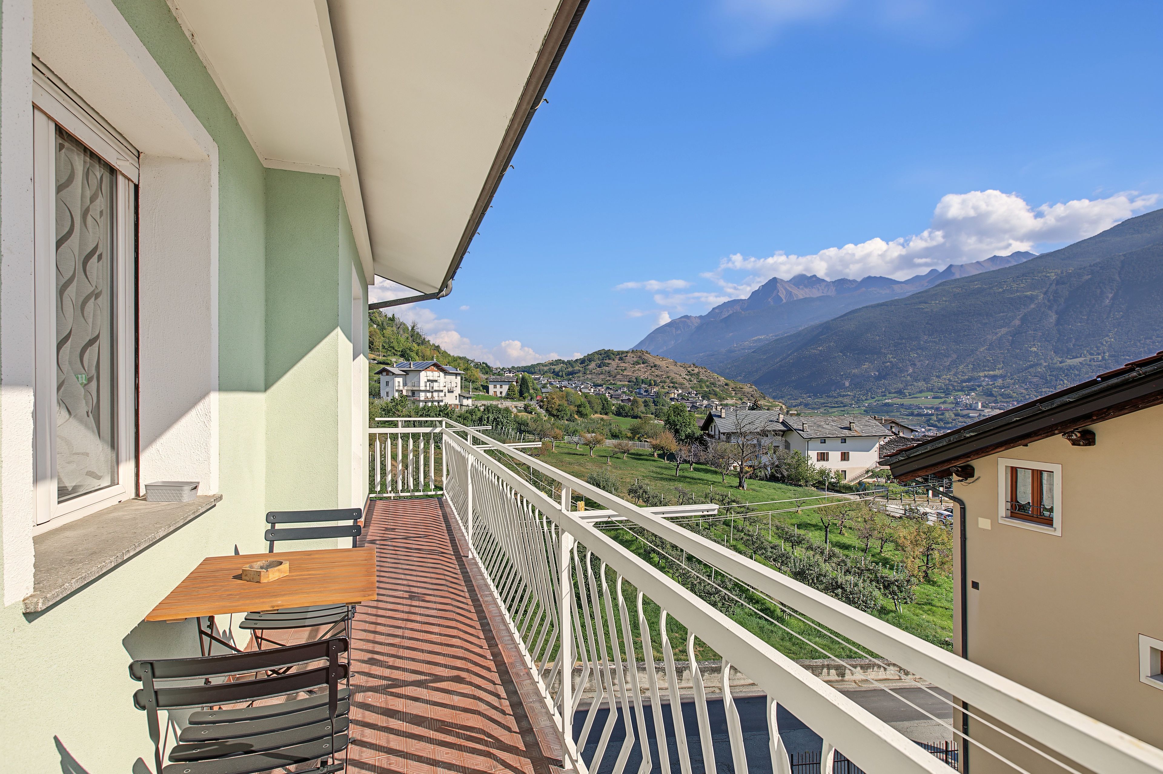 Un balcon avec une table et des chaises, donnant sur un paysage montagneux parsemé de bâtiments.