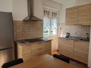 A kitchen with wooden cabinets, a stainless steel range hood, a window with curtains, and a dining table. - Apartment 'Vista Sulla Grivola' with Mountain View, Private Garden and Wi-Fi (Saint-Pierre)