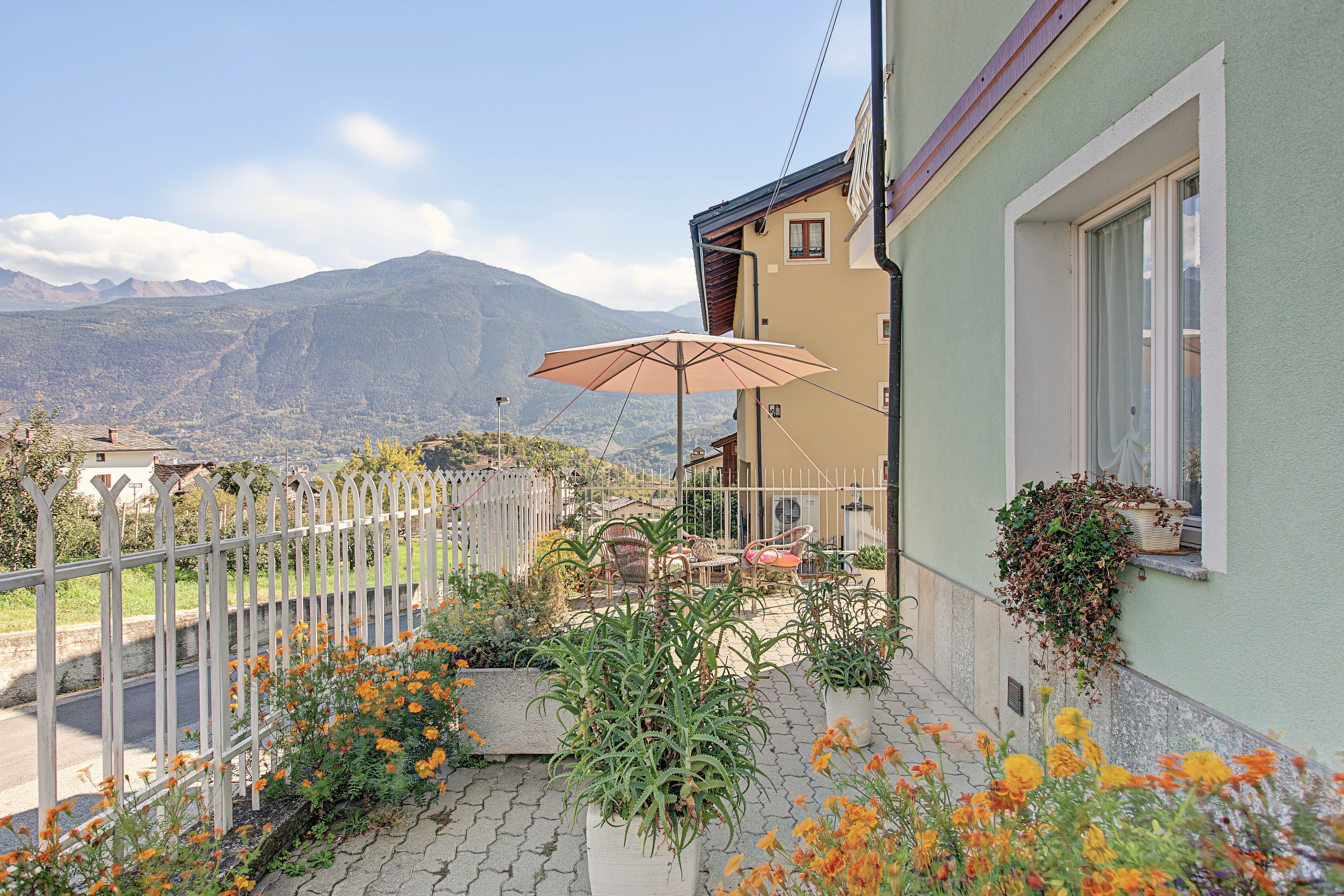 Ein Balkon mit Gartenmöbeln, Blick auf Berge und ein weißer Zaun.