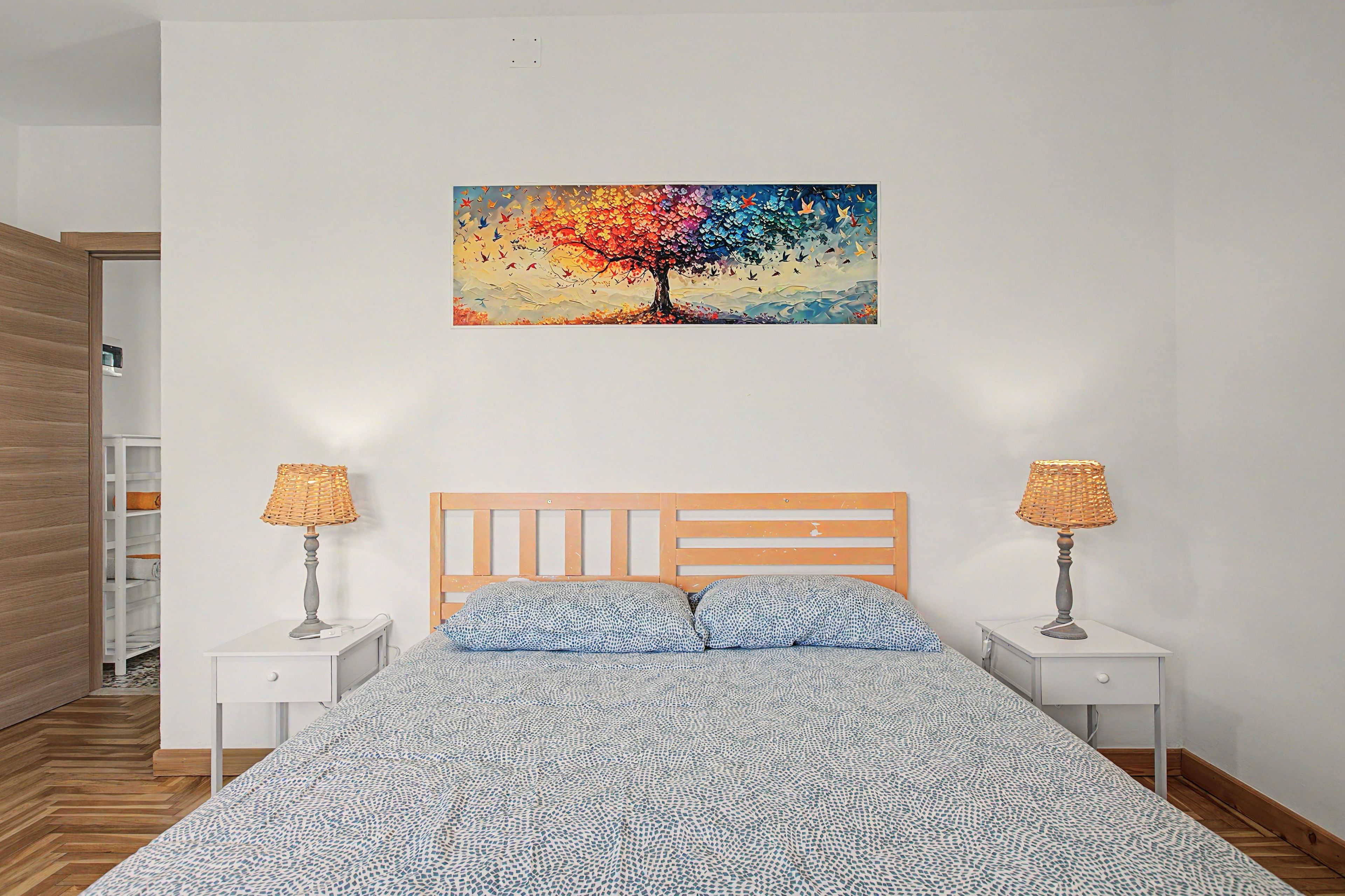 Un dormitorio con una cama, dos mesitas de noche, un cuadro en la pared y un armario de madera.