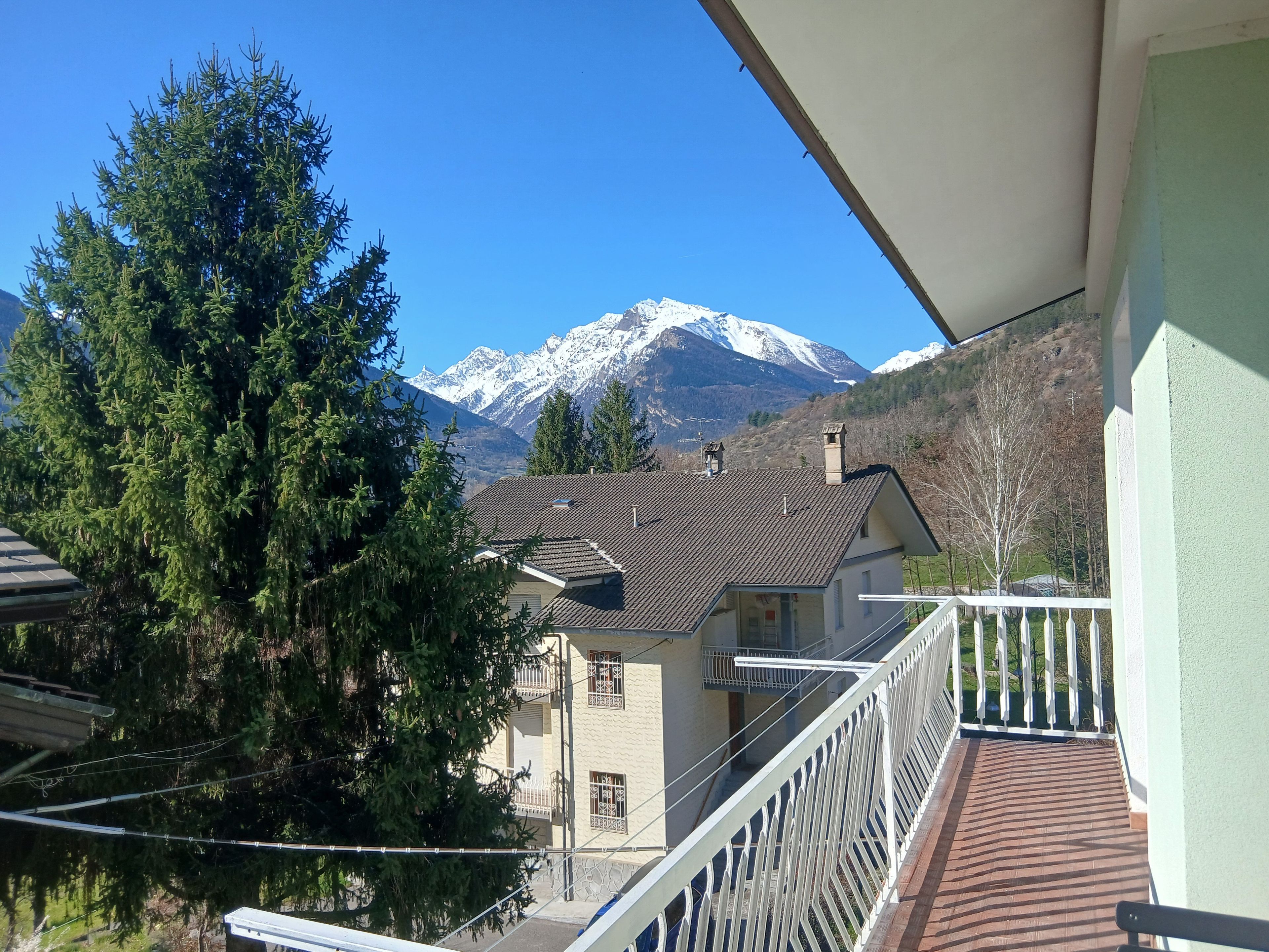 Ein Balkon mit Blick auf einen Berg und ein Haus mit Ziegeldach.