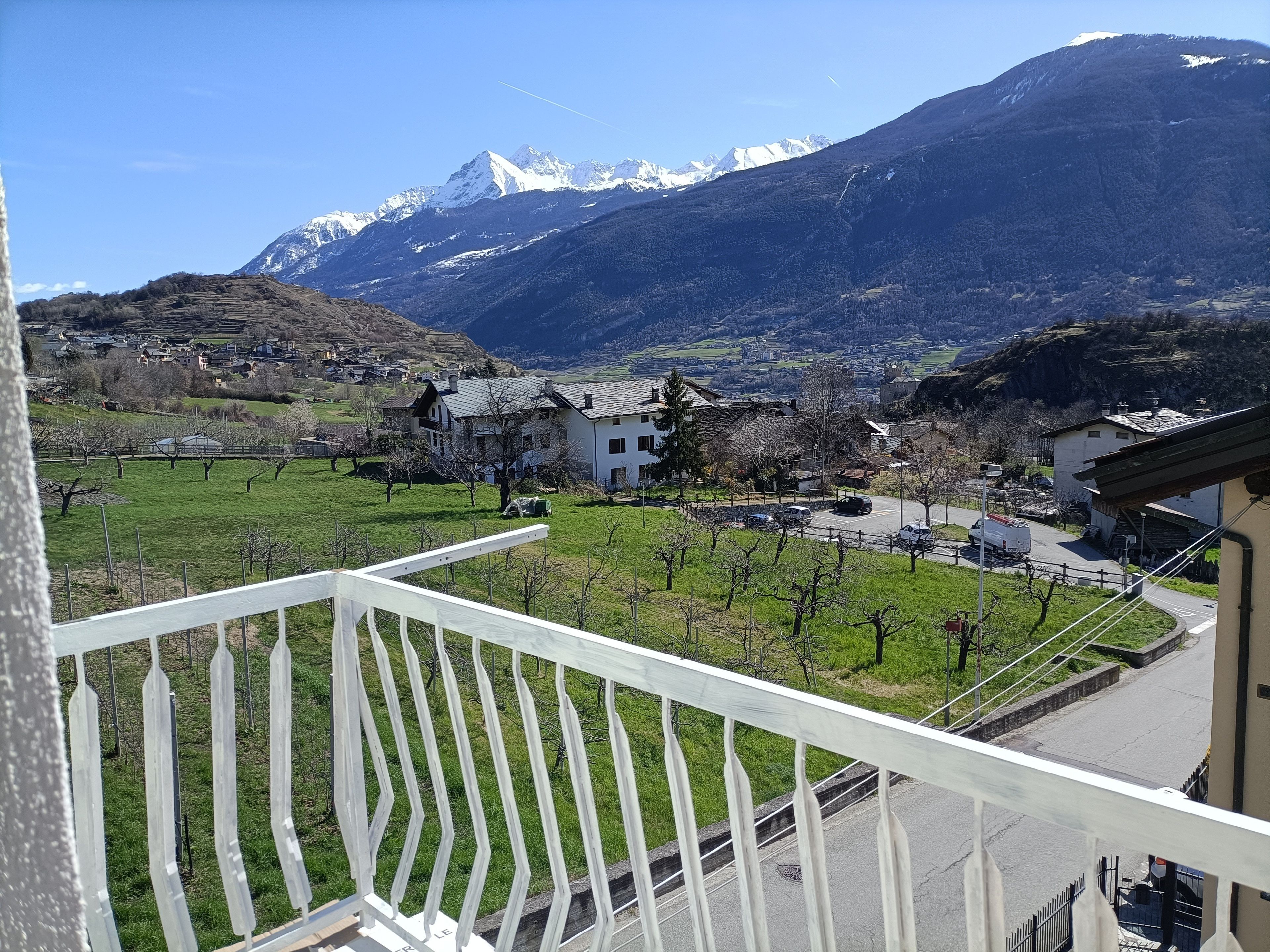 A balcony with a view of a mountainous landscape, a village, and a road with vehicles.