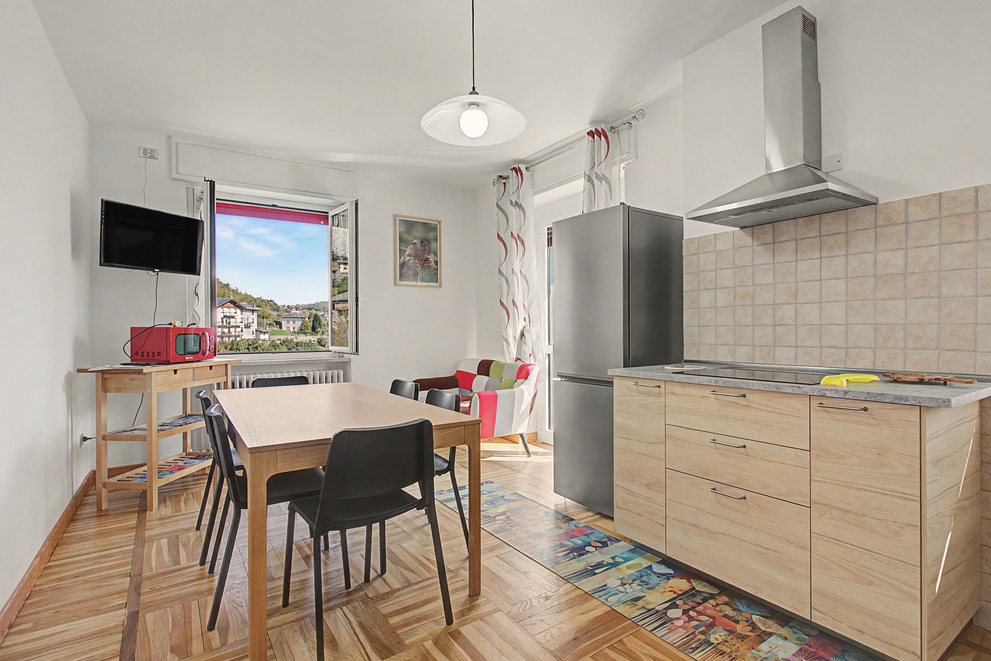 Une cuisine compacte comprenant un coin repas, un four encastré, un réfrigérateur et une fenêtre donnant sur des immeubles.