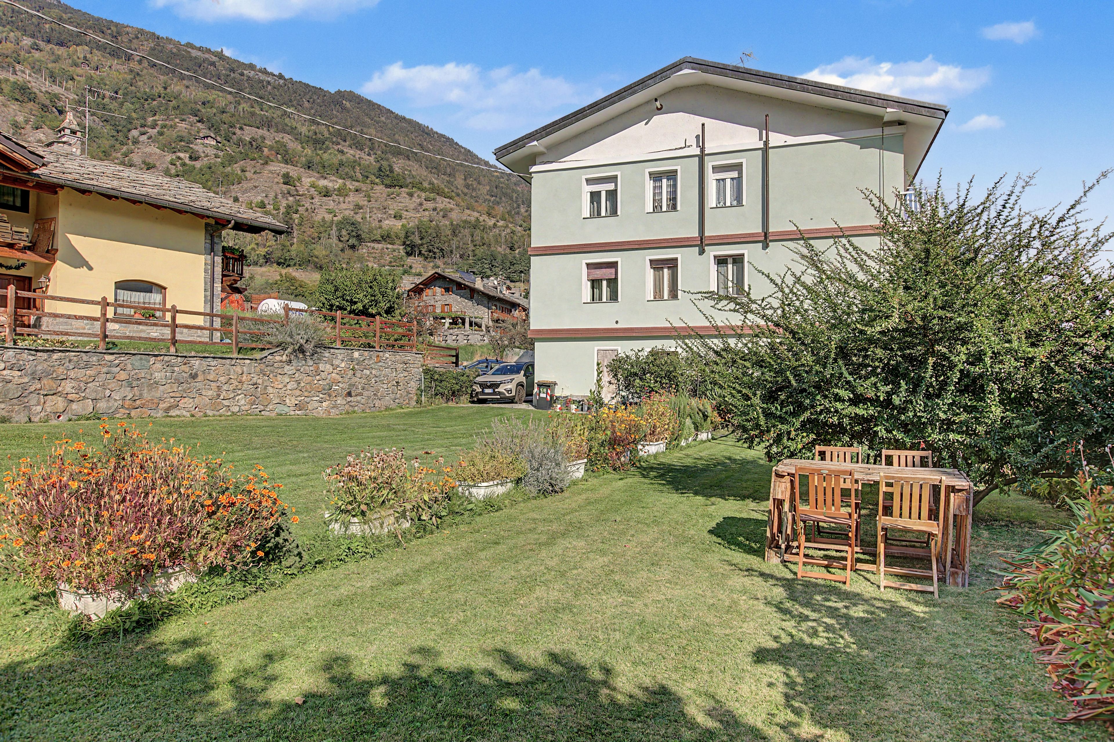 Un edificio de varios pisos con un muro de piedra y un patio cubierto de césped.