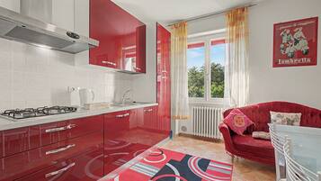 Cocina compacta con armarios rojos, estufa a gas y ventana con cortinas.