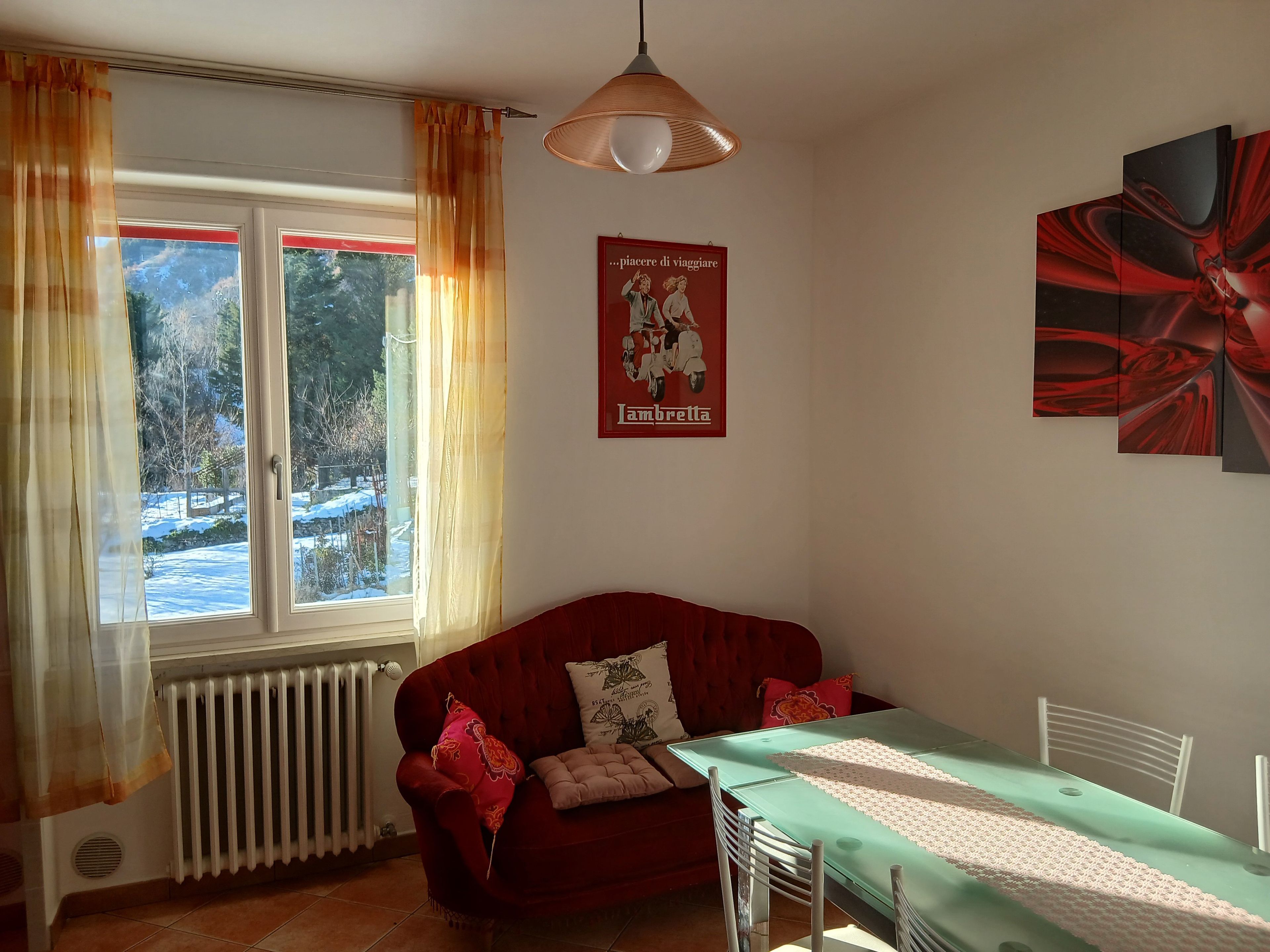 Ein Zimmer mit einem roten Sofa, einem Esstisch mit Stühlen, einem Heizkörper und einem Fenster mit Vorhängen.