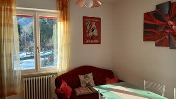 Ein Zimmer mit einem roten Sofa, einem Esstisch mit Stühlen, einem Heizkörper und einem Fenster mit Vorhängen.