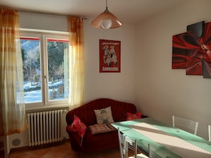 A room with a red sofa, a dining table with chairs, a radiator, and a window with curtains. - Apartment 'Rosemary' with Mountain View, Private Garden and Wi-Fi (Saint-Pierre)