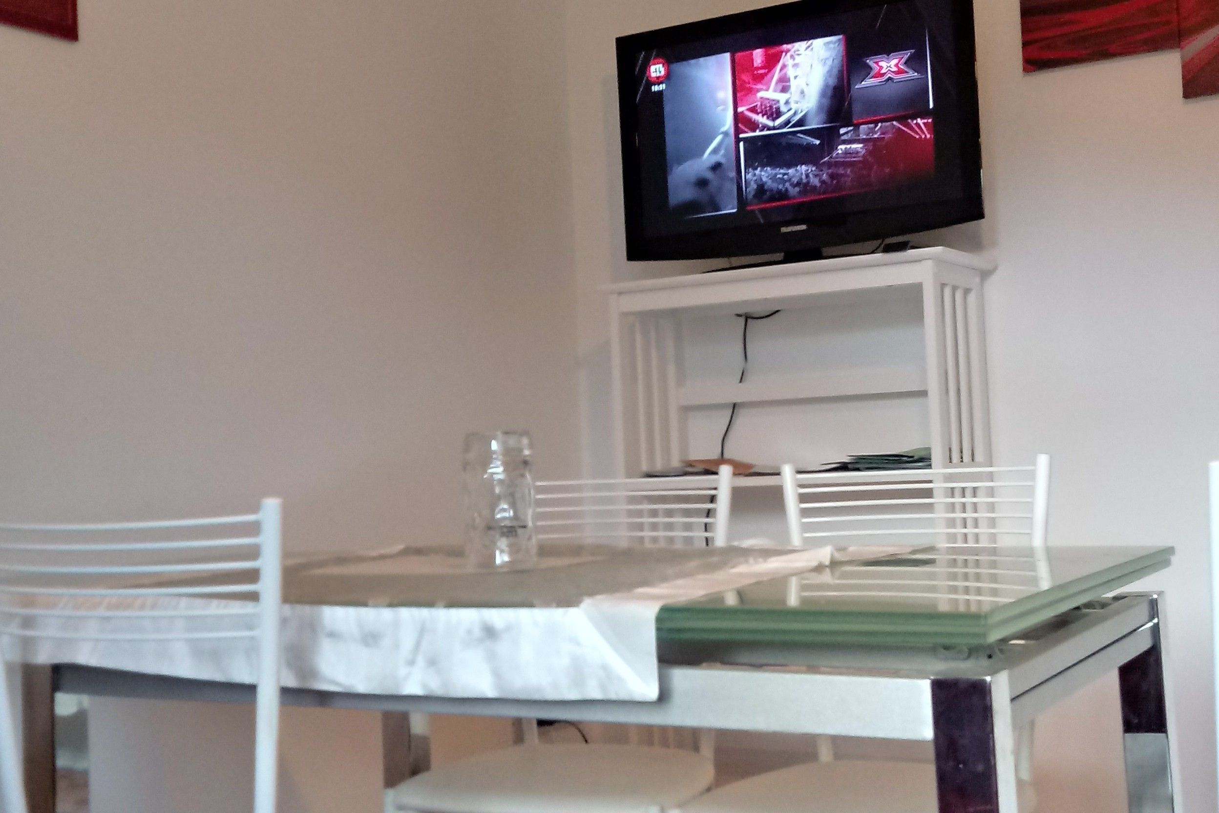 A dining area with a table and chairs, a television mounted on a white cabinet, and a glass on the table.