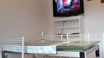 A dining area with a table and chairs, a television mounted on a white cabinet, and a glass on the table.