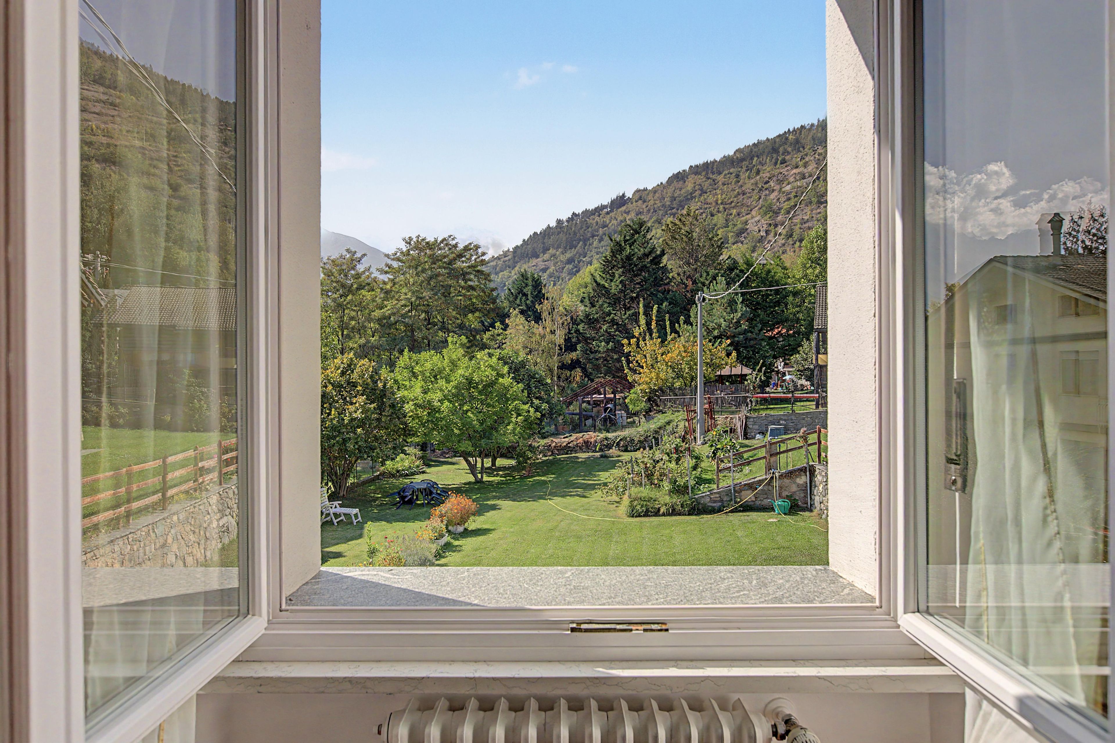Blick aus dem Fenster auf einen Garten mit Rasen, Bäumen und einem Berg im Hintergrund.