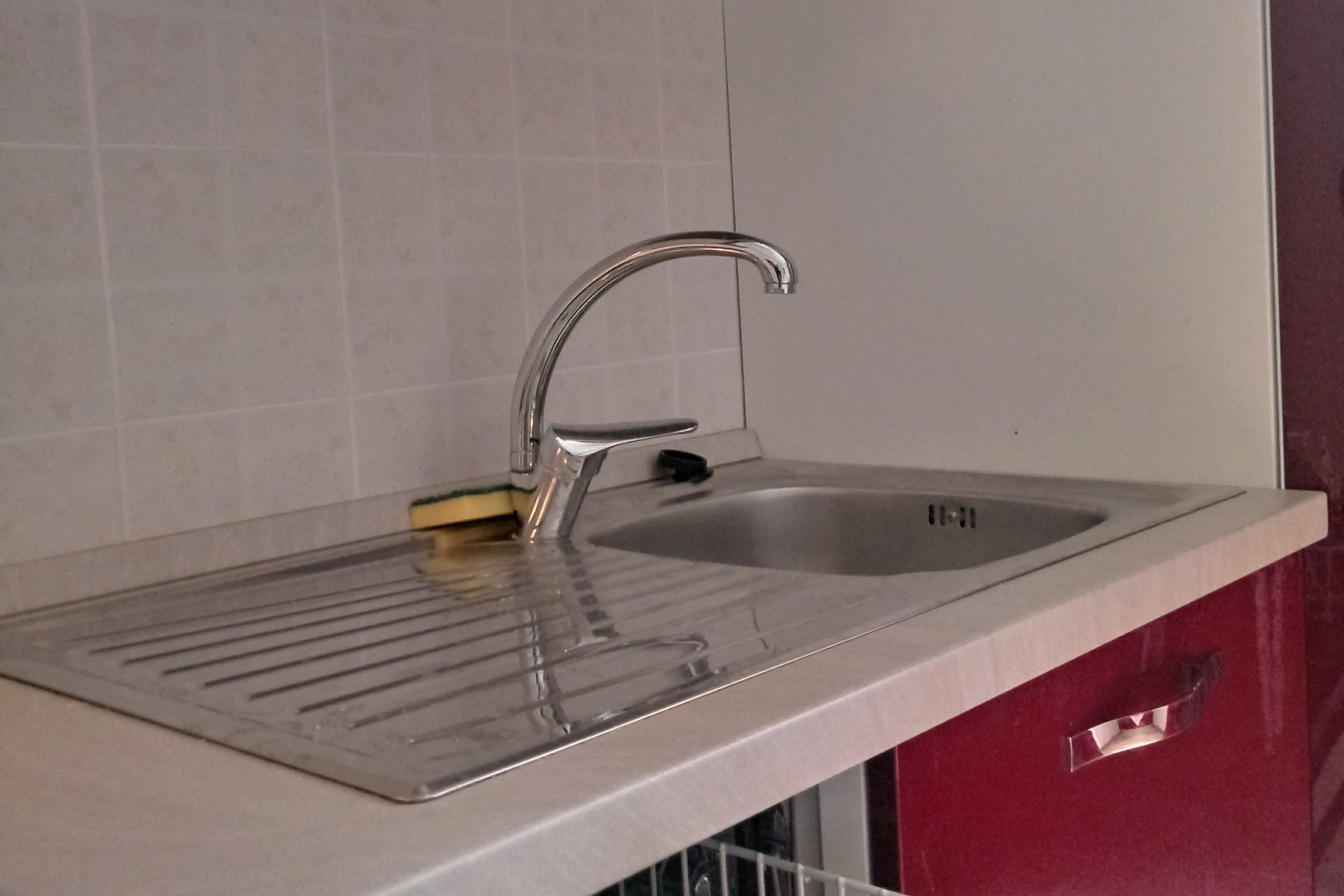 A stainless steel kitchen sink with a single faucet, a soap dish, and a drain stopper.