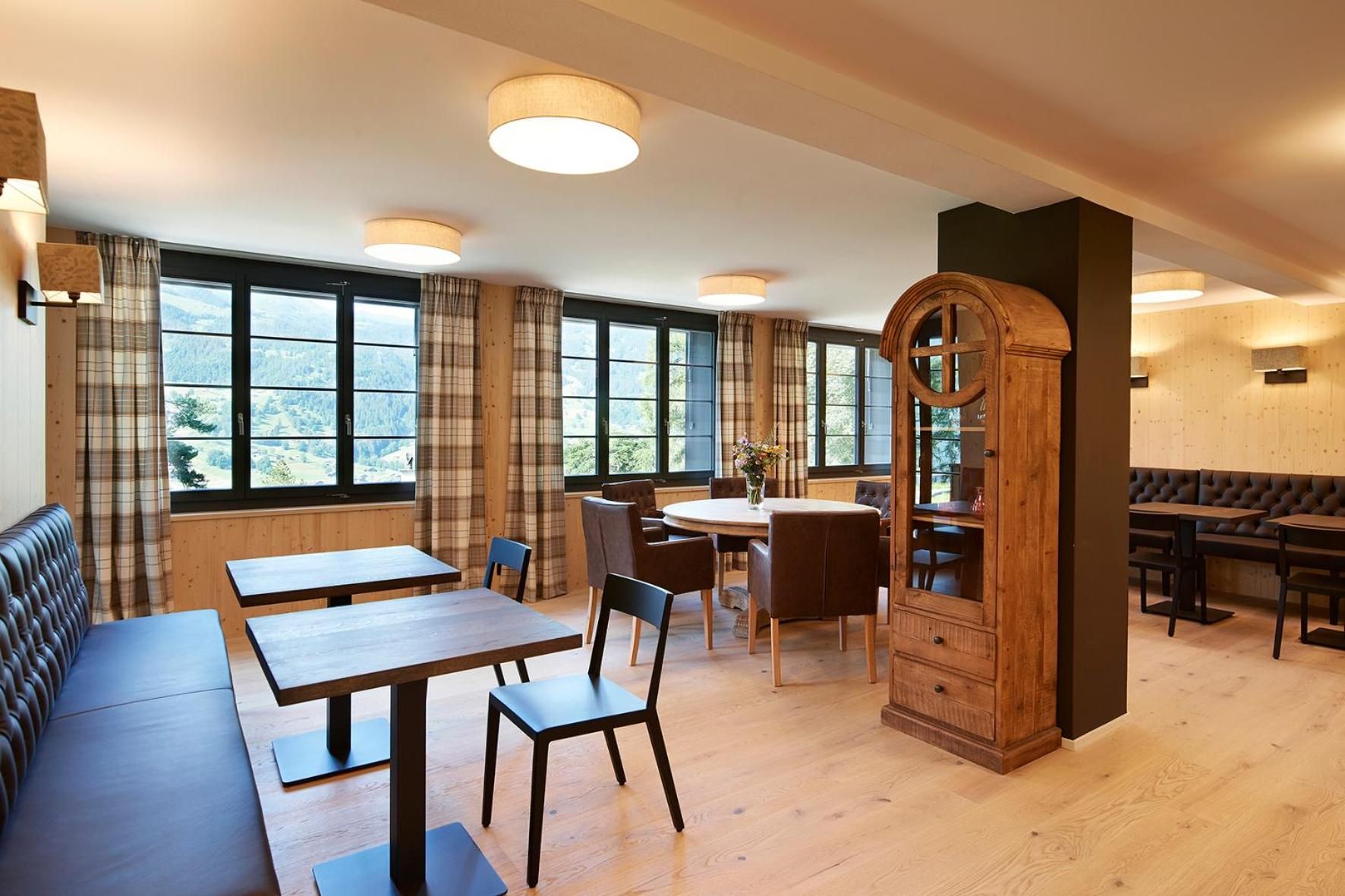 A dining area with wooden tables and chairs, a large wooden cabinet, and a view of the outdoors through large windows.
