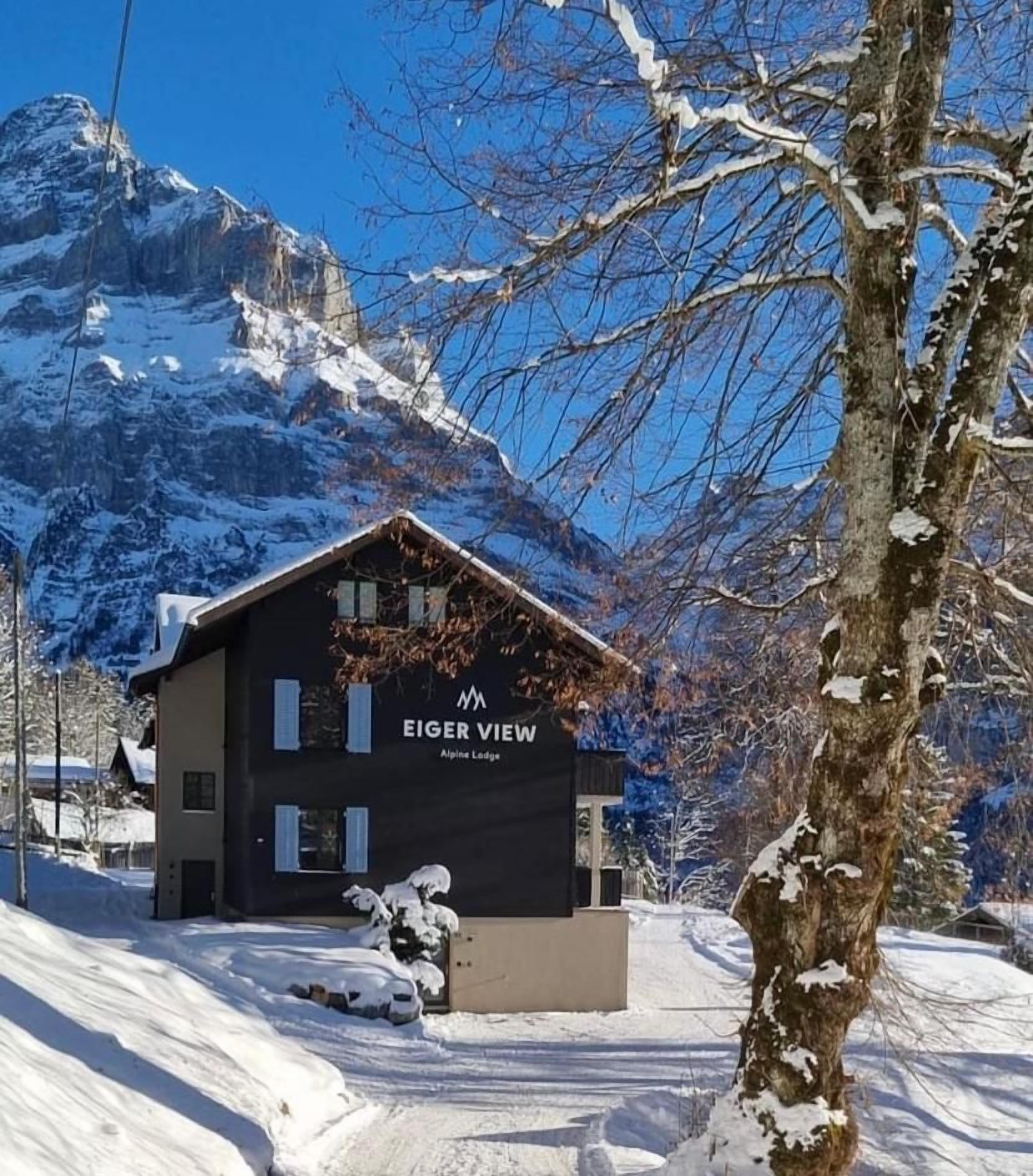 A modern building with 'Eiger View' signage, surrounded by snow-covered mountains.