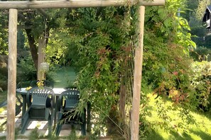 Un espacio al aire libre techado con mesa y sillas, rodeado de exuberante vegetación y una pérgola de madera.