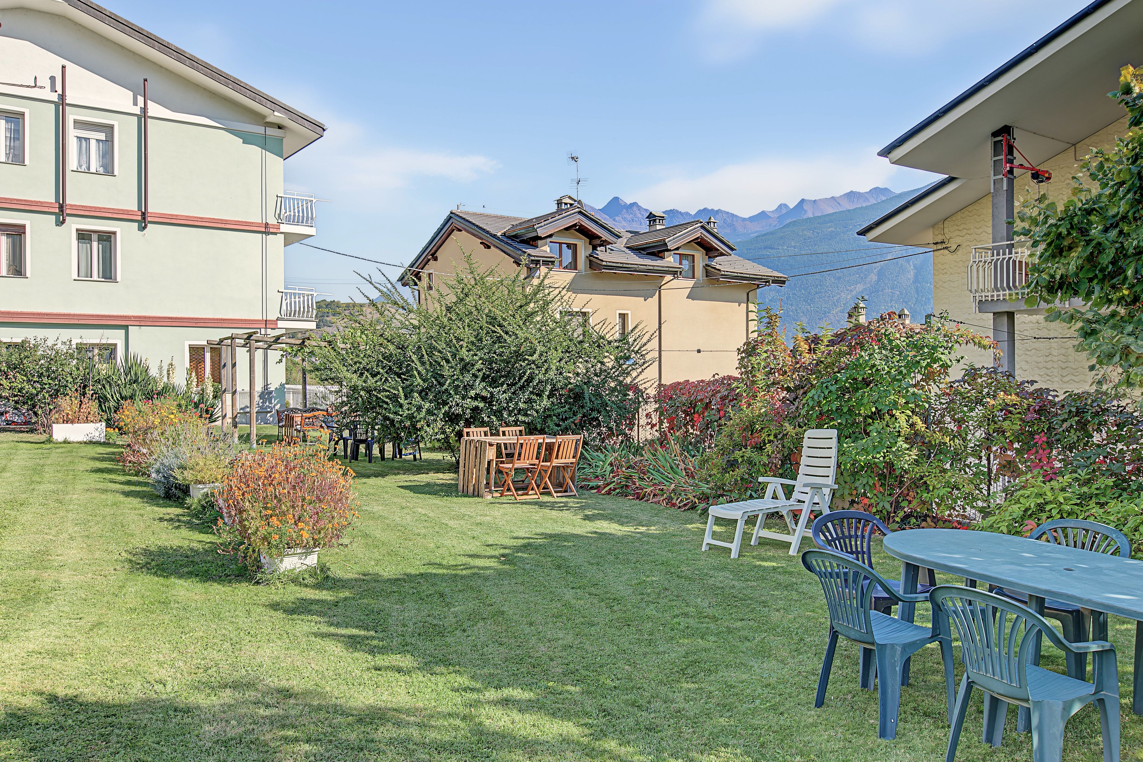 Un giardino curato con tavolo e sedie, circondato da edifici con balconi e vista sulle montagne sullo sfondo.