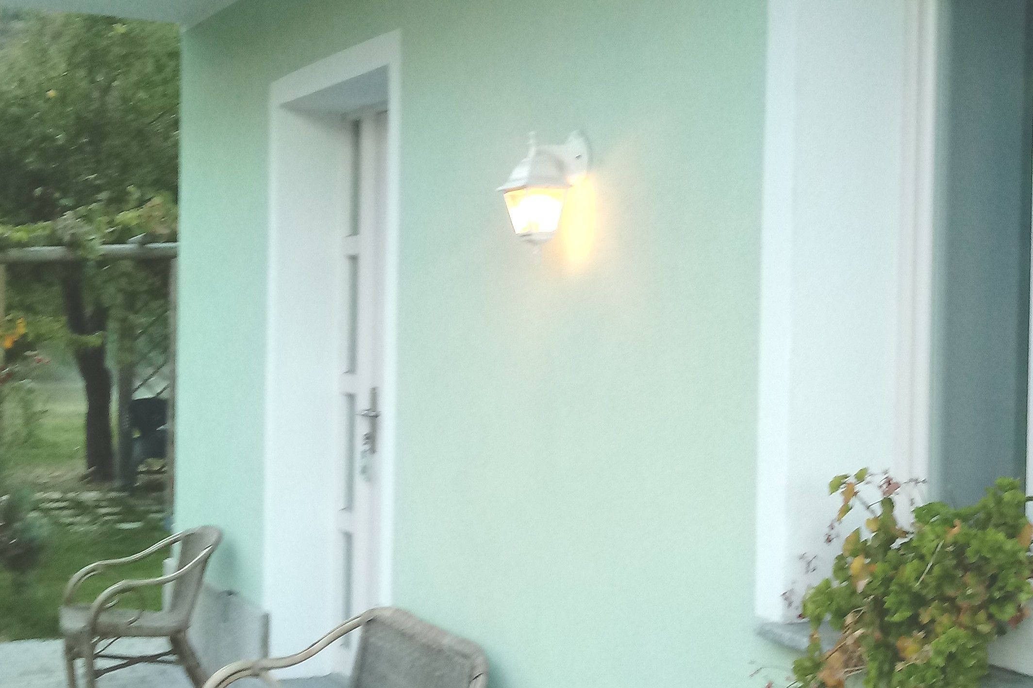 A house with a porch, a door, and a wall-mounted light fixture.
