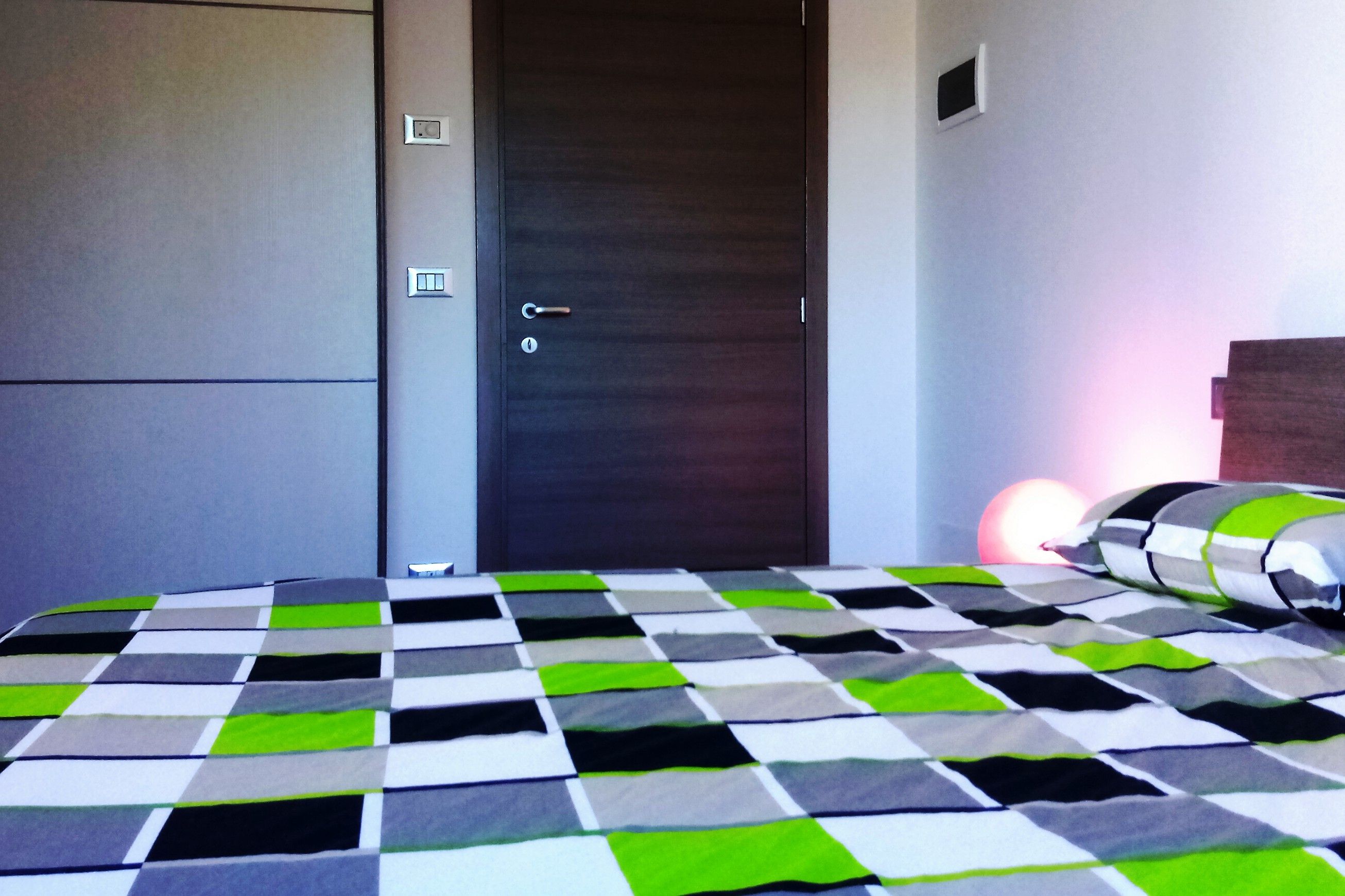 A bedroom with a checkered bedspread, a dark door, and a small window.