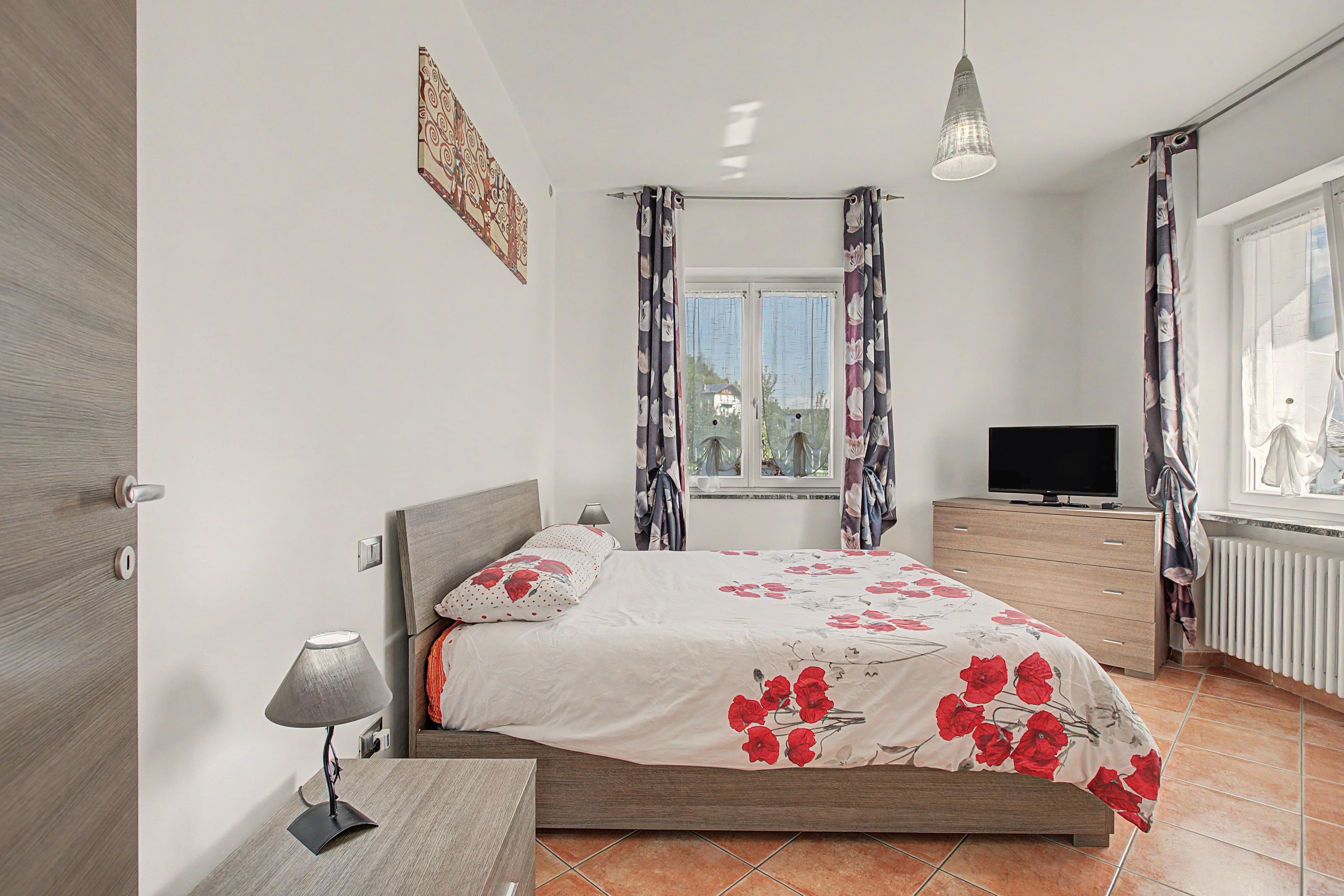 Una camera da letto con un letto, una TV, una lampada e una finestra con tende.