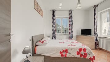 Una camera da letto con un letto, una TV, una lampada e una finestra con tende.