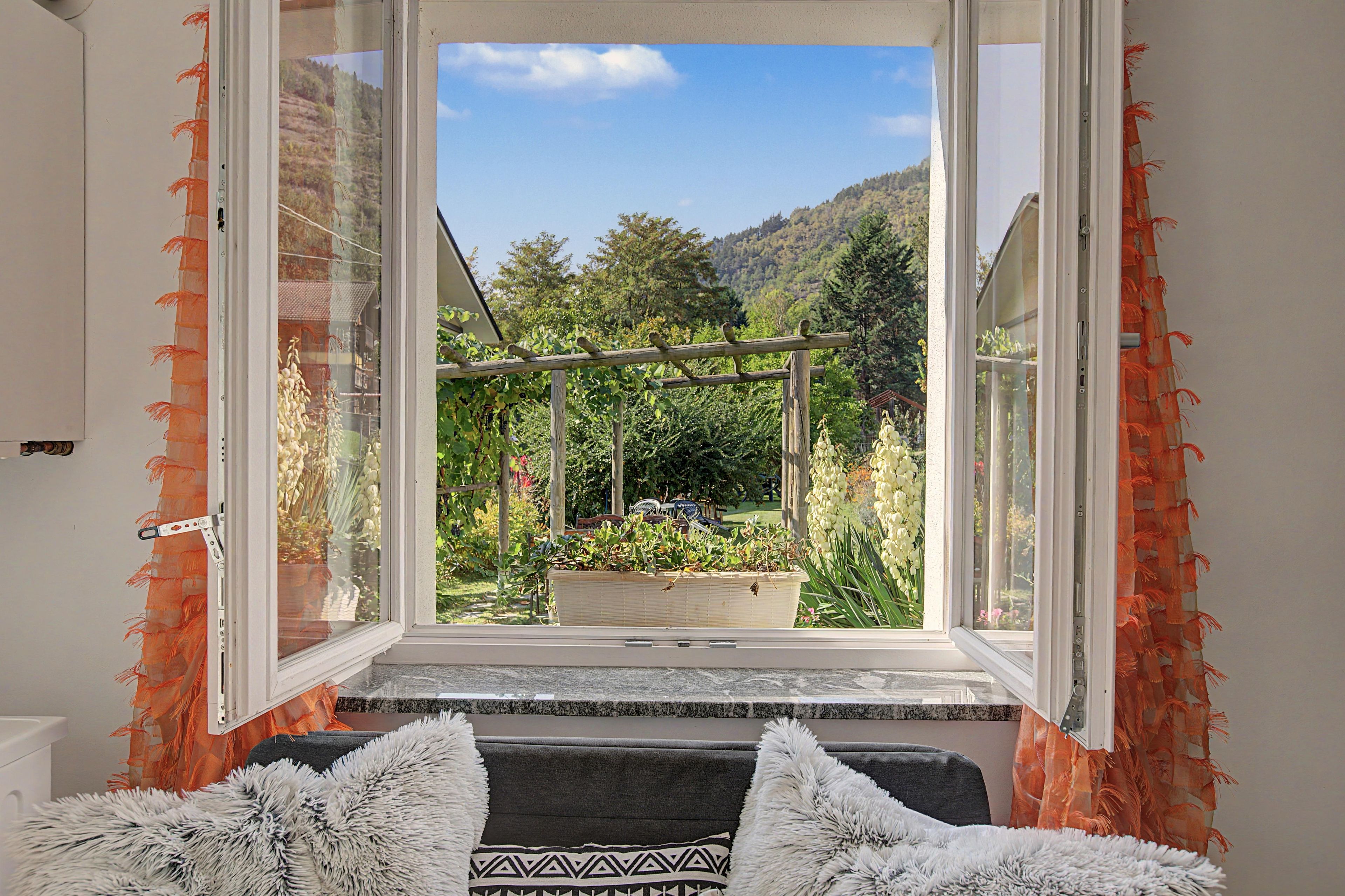 Una habitación con un ventanal grande que da a un jardín con una pérgola de madera y una jardinera.