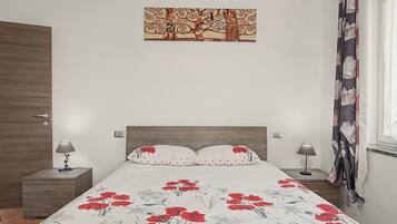 Une chambre à coucher comprenant un lit, deux tables de chevet, une commode, une œuvre d’art accrochée au mur et une fenêtre avec des rideaux.