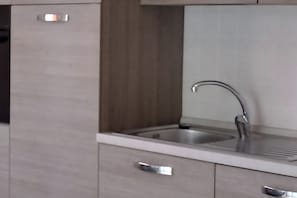 Una cuina moderna amb un vàter d'acer inoxidable, un armari de fusta i un taulell blanc.