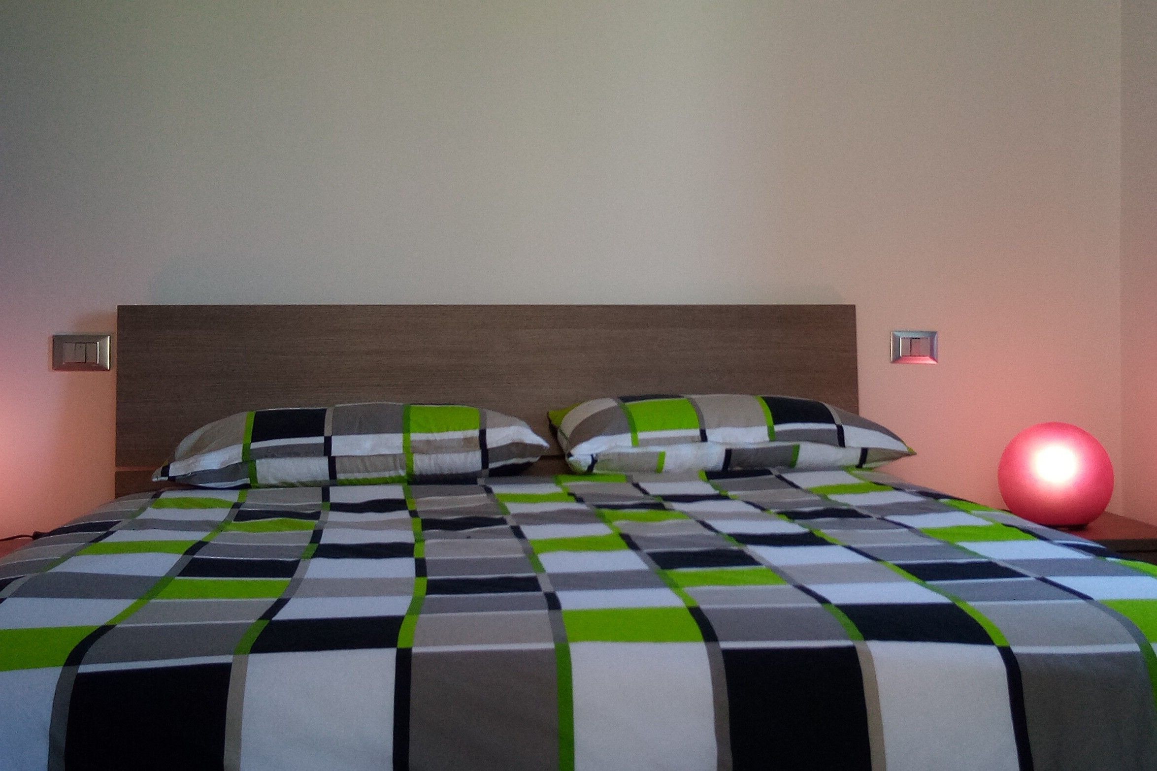 A bed with a checkered bedspread, two pillows, a nightstand, and a red spherical object on the wall.