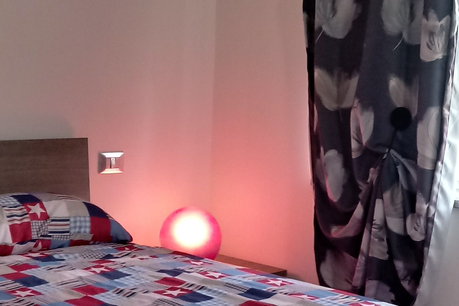 Un dormitorio con una cama, una lámpara de pared y una cortina.