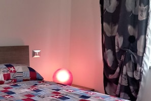 Un dormitori amb un llit, una làmpada penjada a la paret i una cortina.