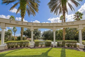 A sign with the words 'Emerald Island' under a white archway, surrounded by palm trees and well-maintained grass. - Emerald Island Escape | Luxury Stay Near Disney (Kissimmee)