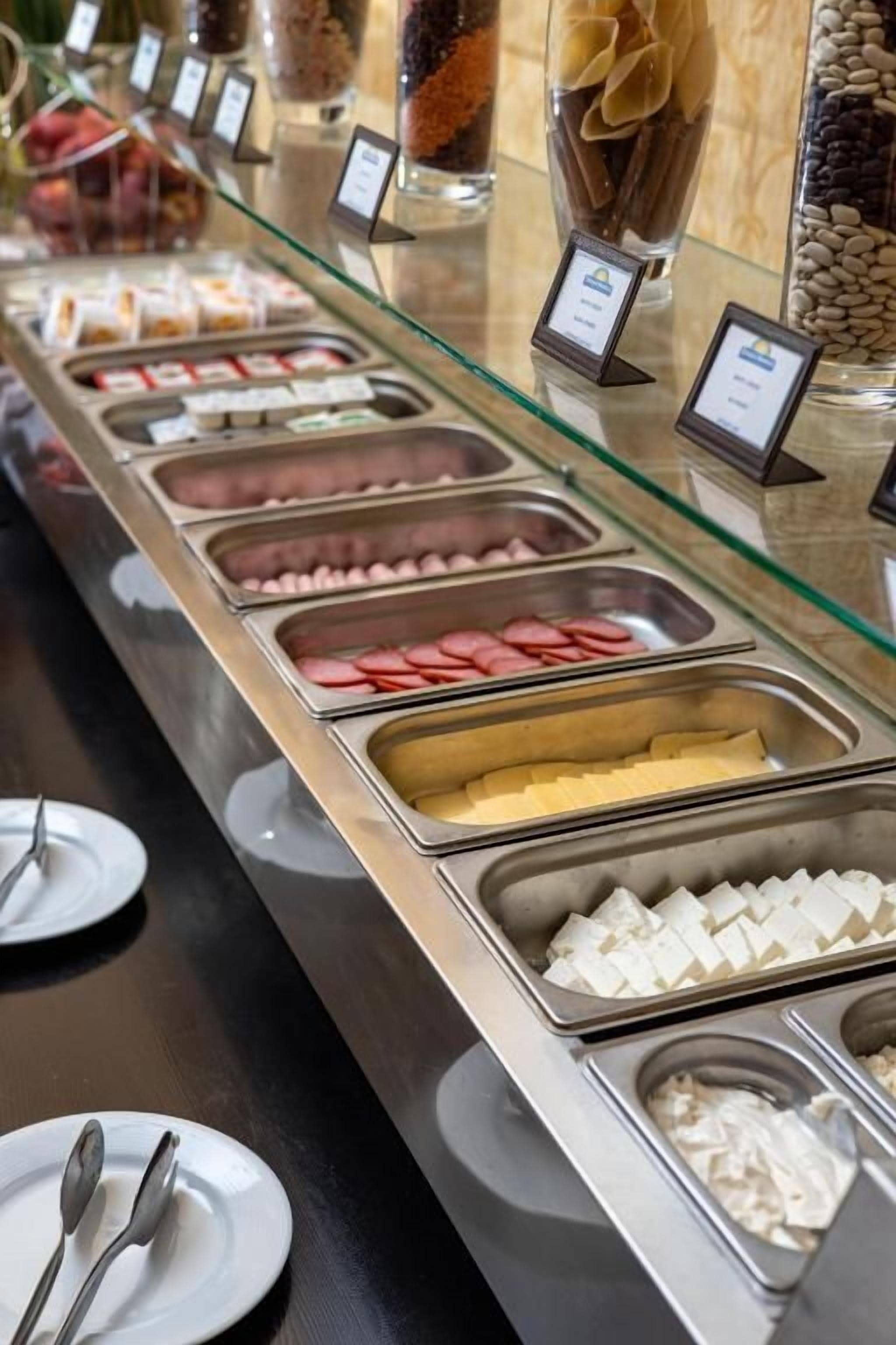 A buffet with various food items in separate containers, including meats, cheeses, and other prepared dishes.