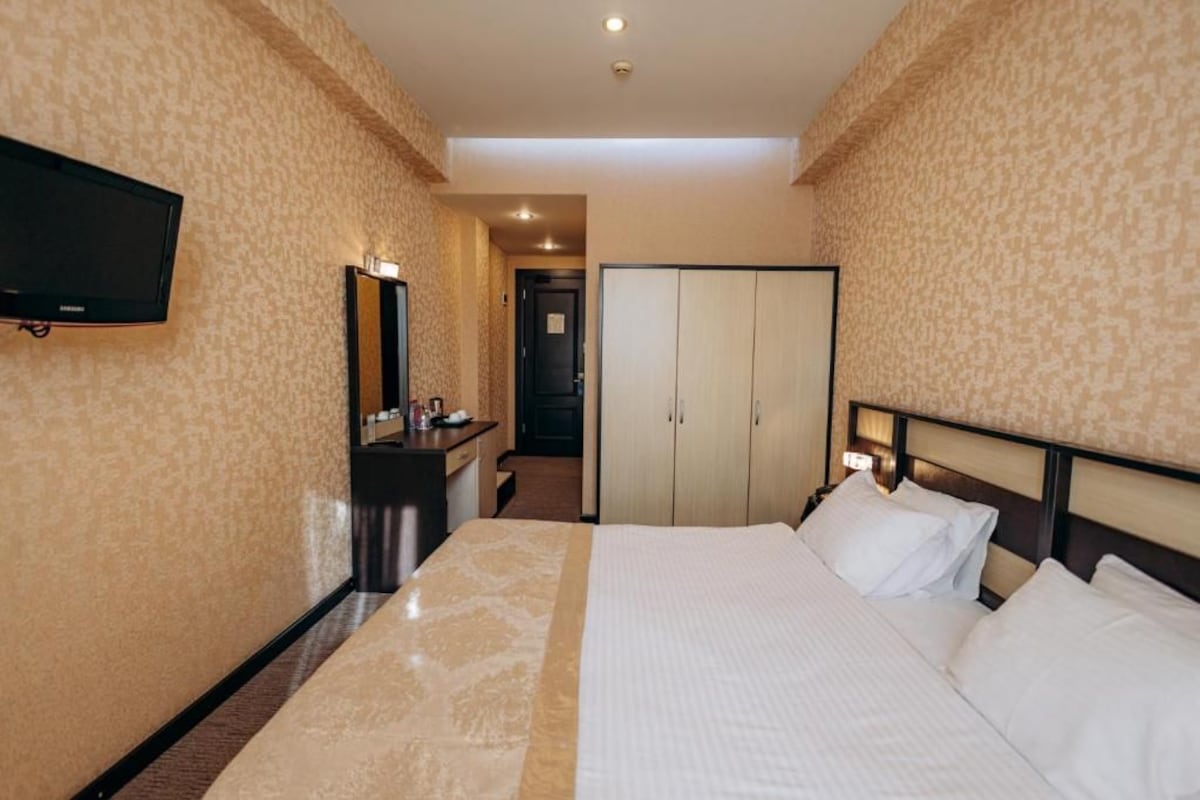 A hotel room with a bed, a TV mounted on the wall, a wardrobe, and a mirror.