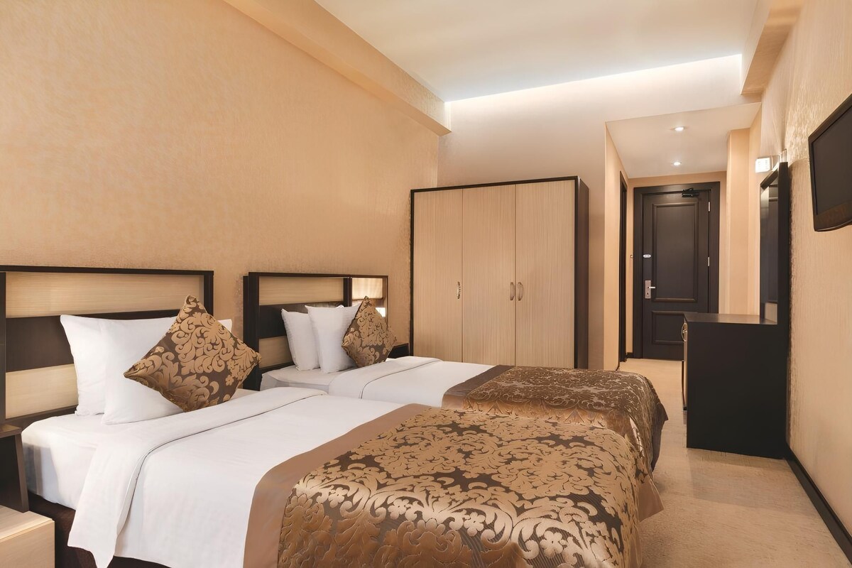 A hotel room with two beds, a wardrobe, a desk, and a television.