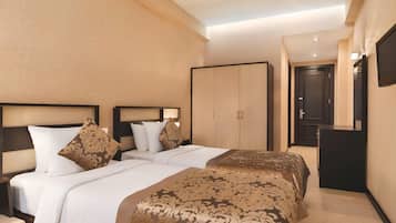 A hotel room with two beds, a wardrobe, a desk, and a television.
