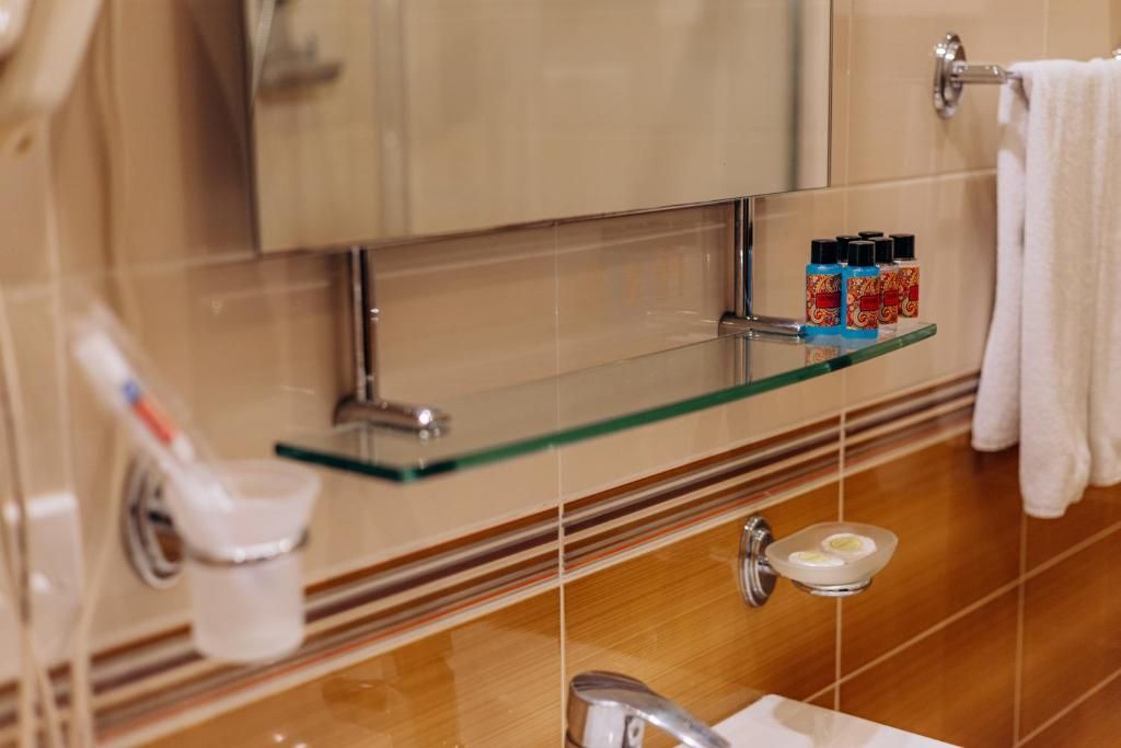Un baño con repisa de vidrio para artículos de aseo, toallero y espejo.