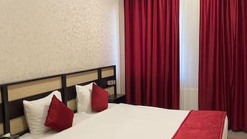 A hotel room with a bed, a nightstand, a drawer, and a window with red curtains.