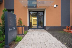 Een gebouw-ingang met een glazen luifel, een metalen bord met een nummer en een geplaveid voetpad.
